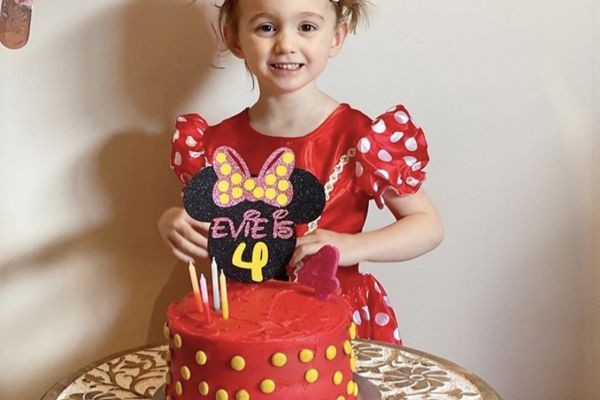 A girl standing behind her Minnie Mouse-themed cake and cake topper