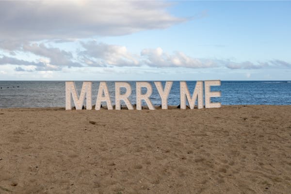 A marry me sign on a beach with large letters